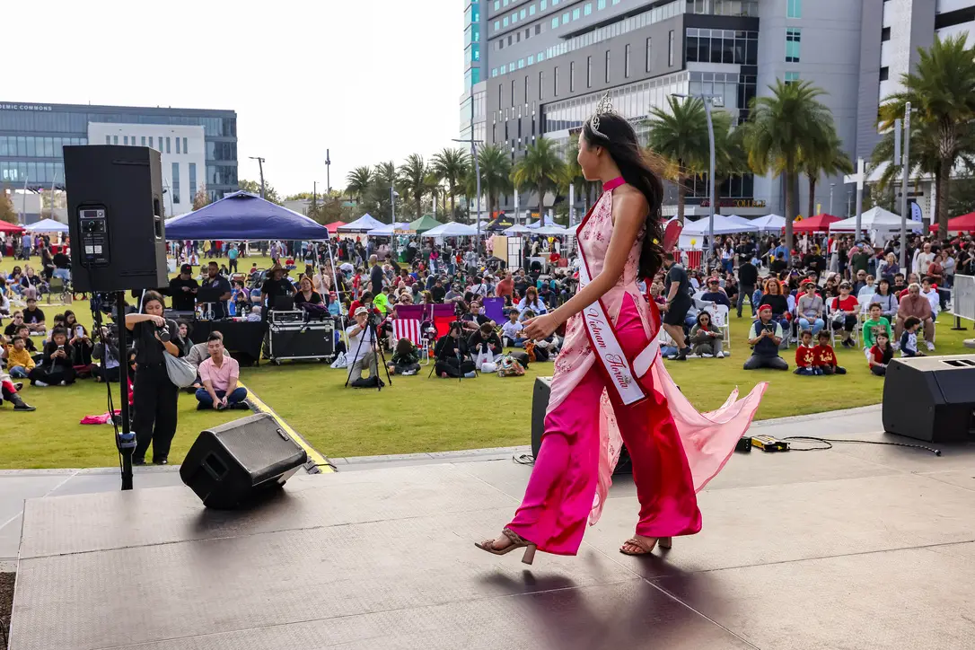 A performer in a pink gown crosses the Celebrate Lunar main stage in front of the festival crowd and the Downtown Orlando skyline