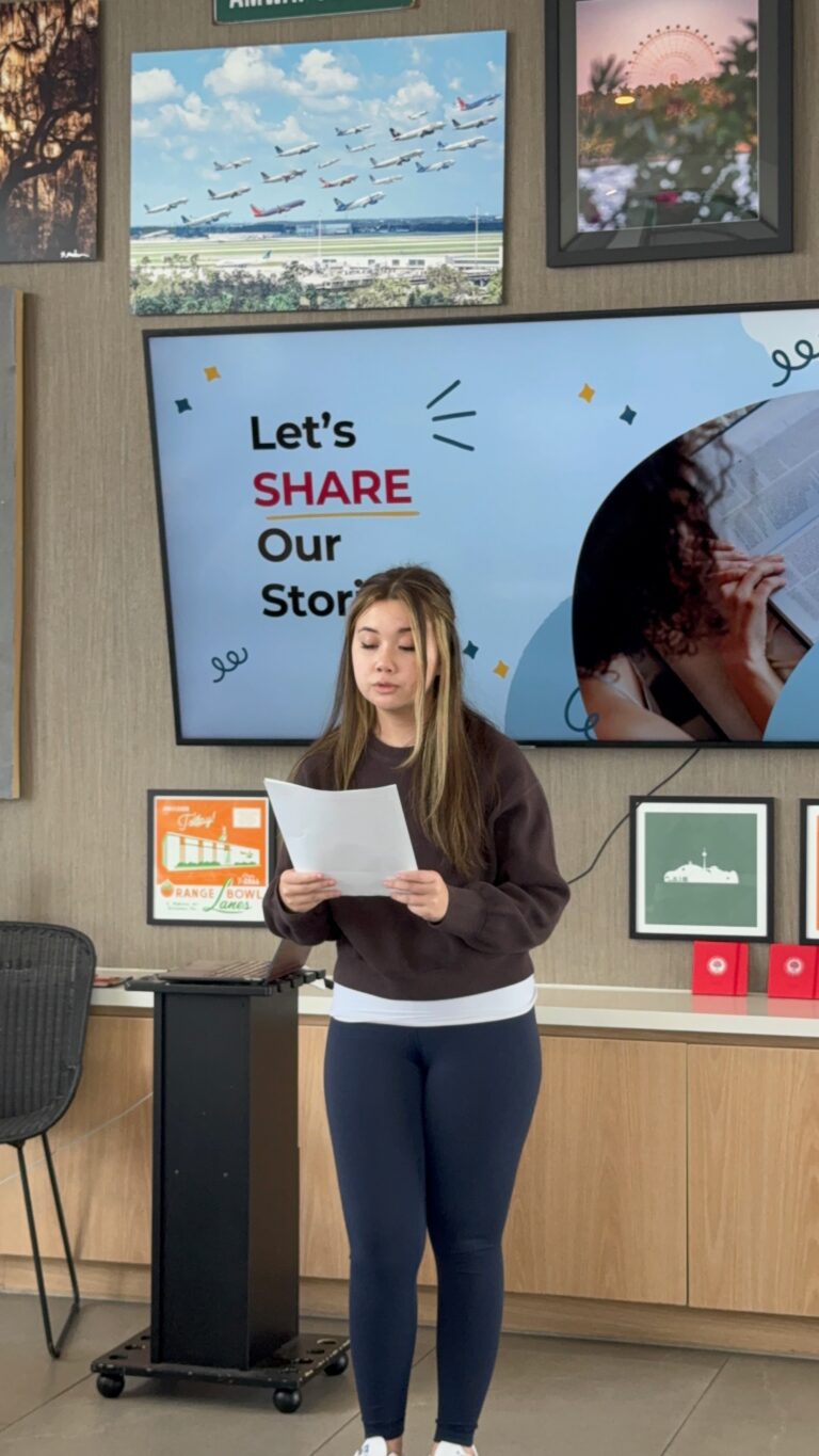 A student reads their finished piece aloud in front of the Let's Share Our Stories slide