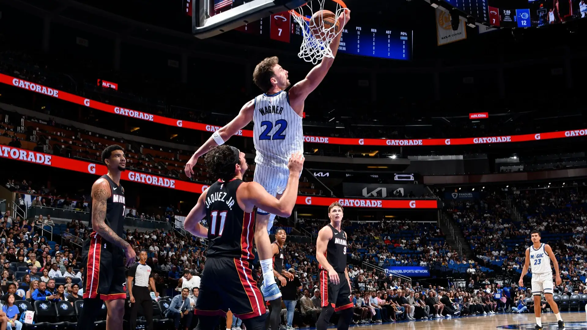 Orlando Magic player in a pinstripe jersey dunks over a Miami Heat defender at Kia Center