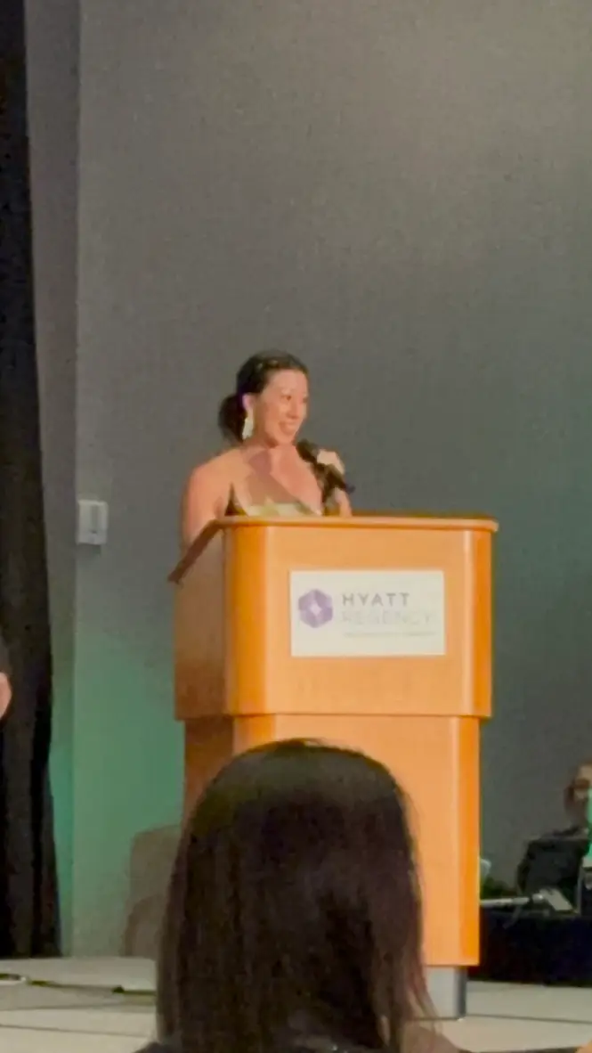 Maxine Sudarma speaking at a Hyatt Regency podium during the AACC awards gala