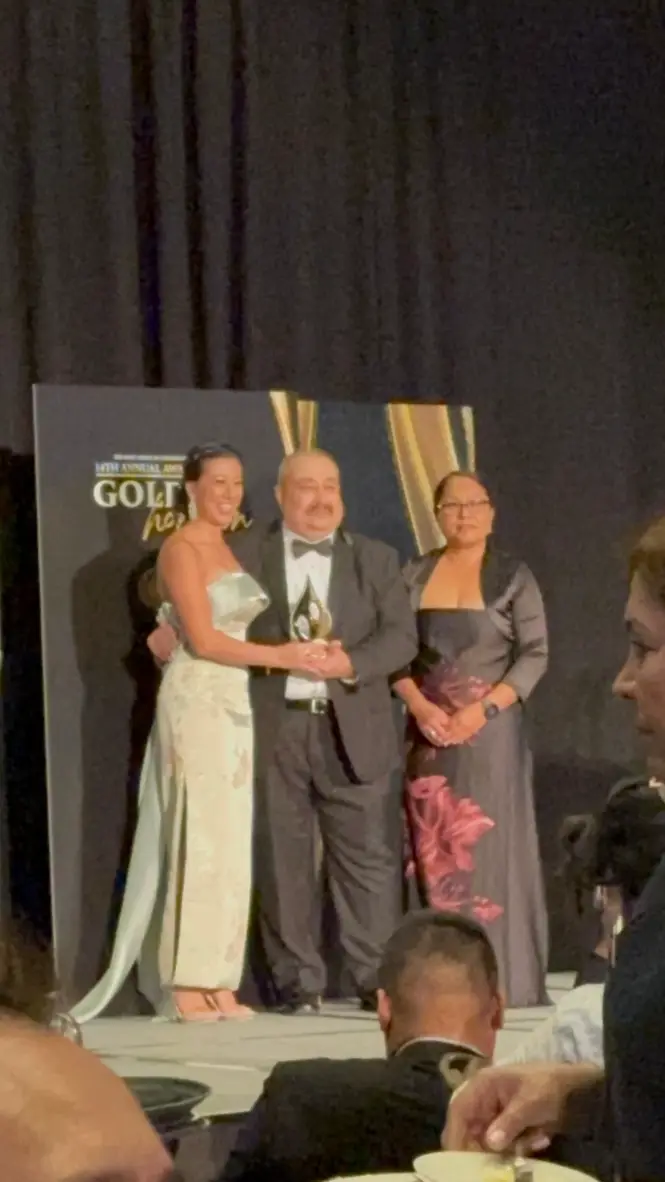 Maxine Sudarma holding the AACC 2026 Community Impact Award on stage at The Golden Horizon gala